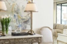 a neutral refined space with an inlay console table, an upholstered bench, a neutral antique chair and some table lamps