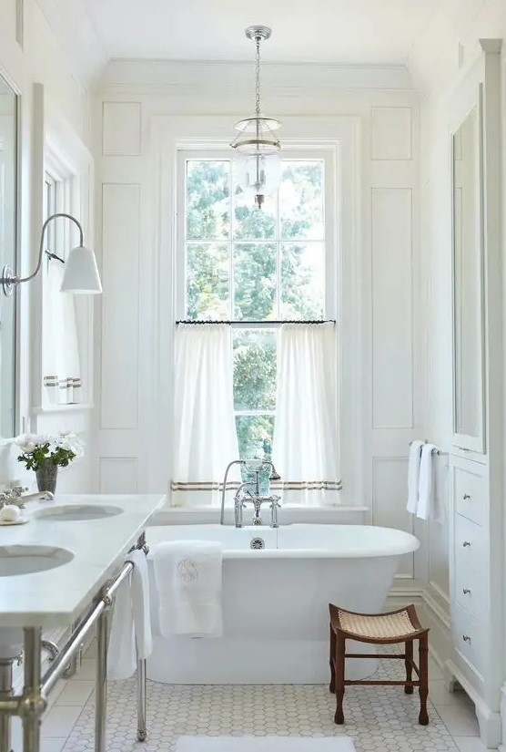 a neutral vintage bathroom with trim, an oval tub, a double-hung window, curtains, a double sink on a metal stand