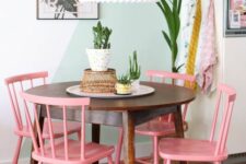 a pastel dining nook with a color block accent wall, a stained table and pink chairs, a pendant lamp is a cool space