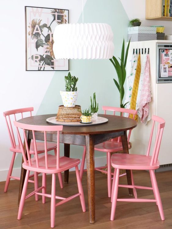 a pastel dining nook with a color block accent wall, a stained table and pink chairs, a pendant lamp is a cool space
