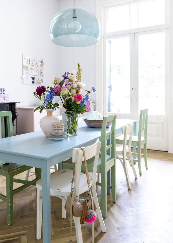 a pastel dining room with a blush sideboard, a blue table, green chairs and a blue pendant lamp is a stylish and cool space