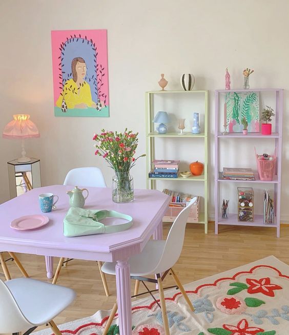 a pastel dining room with matching pastel storage units, a pink dining table and white chairs, a colorful rug and artwork