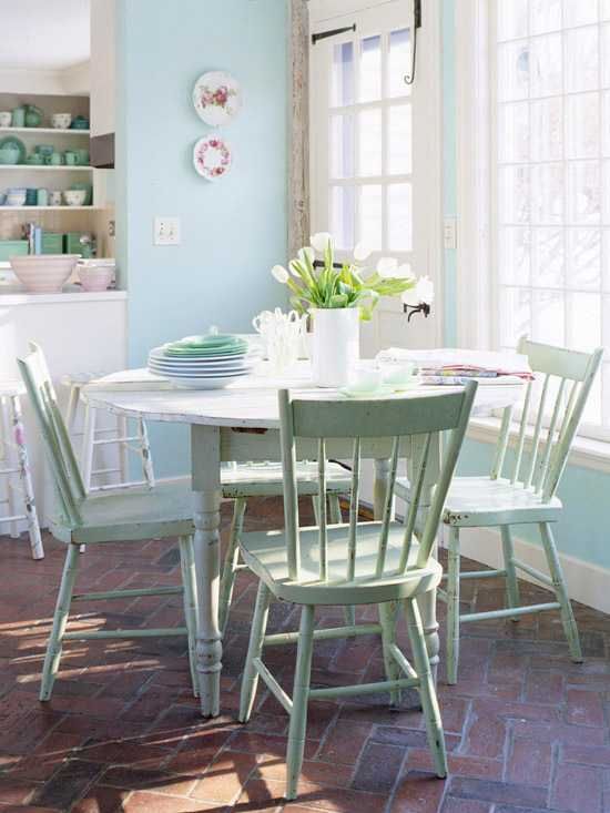 a pastel dining space by the window, with a round table, green chairs, blue walls and decorative platters