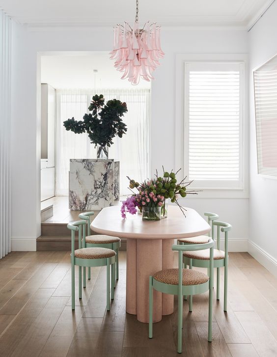 a pastel dining space with a pink oval table and green and pink curved chairs plus a catchy pink chandelier is super chic