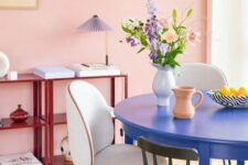 a pastel pink dining room with red storage units, a bold blue round table, mismatching chairs and a pendant lamp