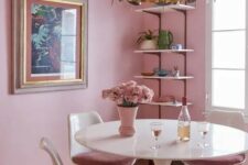 a pink dining room with open shelves, a round table, mauve chairs, a cool chandelier and a bold artwork
