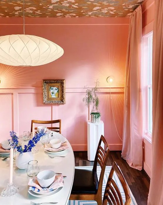 a pink dining space with a printed ceiling, paneling, an oval table, stained chairs and some pretty art
