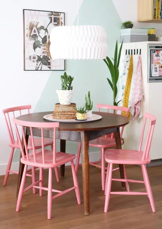 a pretty dining nook with a color block green and white wall, a stained round table, pink chairs, a pendant lamp and potted plants