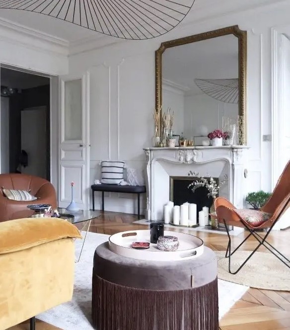 a pretty modern French chic living room with a French fireplace, leather and velvet furniture of earthy tones and an oversized mirror