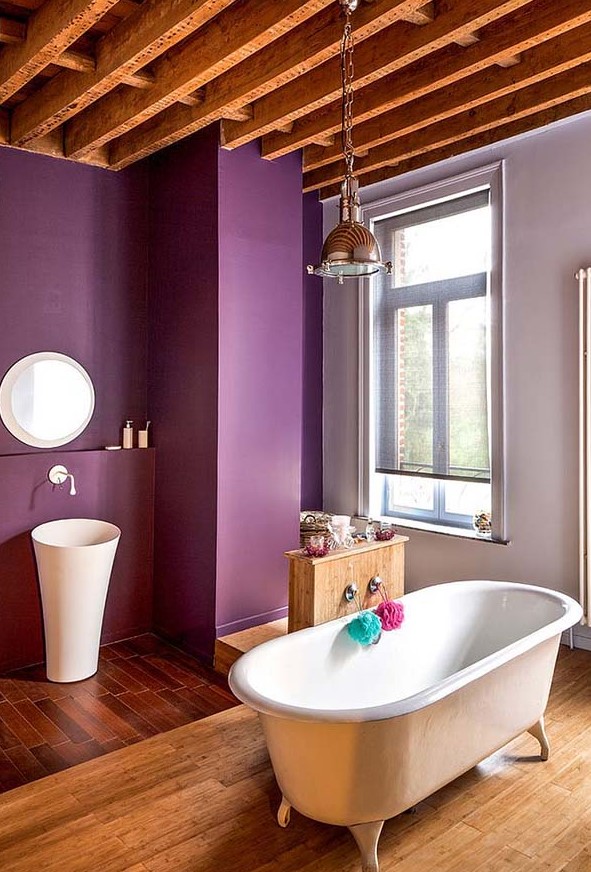 a purple farmhouse bathroom with a wooden ceiling with beams, a pendant lamp, a free-standing sink and a vintage bathtub