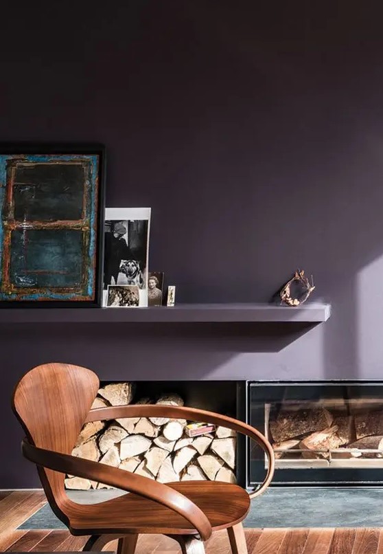 a refined living room with a deep purple accent wall, firewood storage and a built in fireplace, a floating shelf with decor