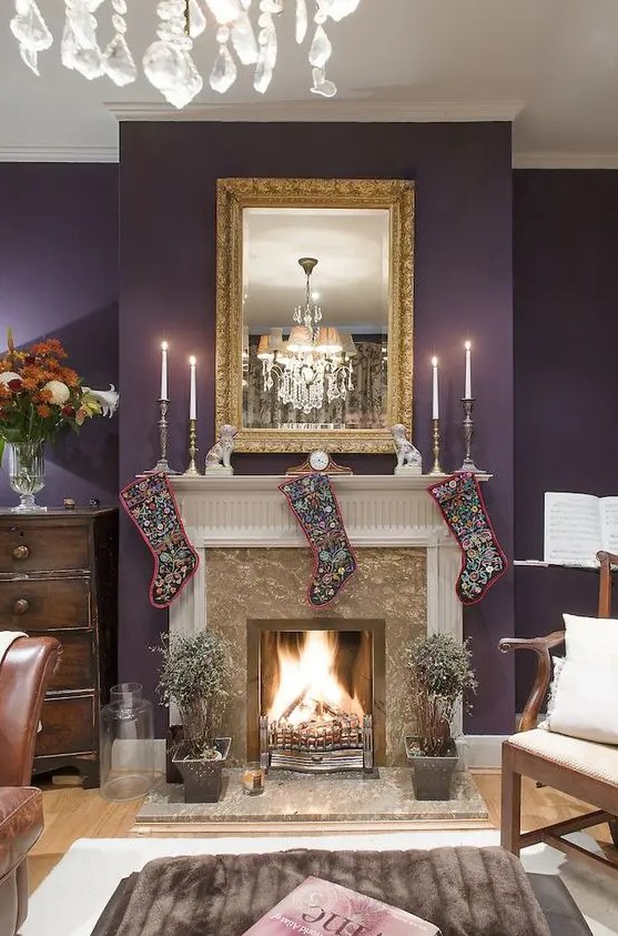 a refined living room with an aubergine accent wall, a fireplace, a mirror in a vintage frame, stockings and a crystal chandelier