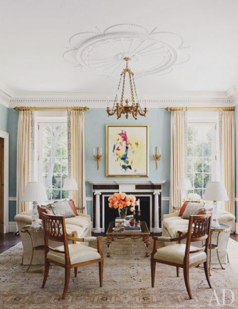 a refined living room with blue walls, a non-working fireplace, neutral seating furniture, antique chairs, a chic gilded chandelier