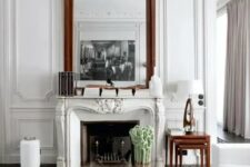 a refined living room with molding and an ornated French fireplace, white seating furniture, a coffee table, a couple of oversized mirrors