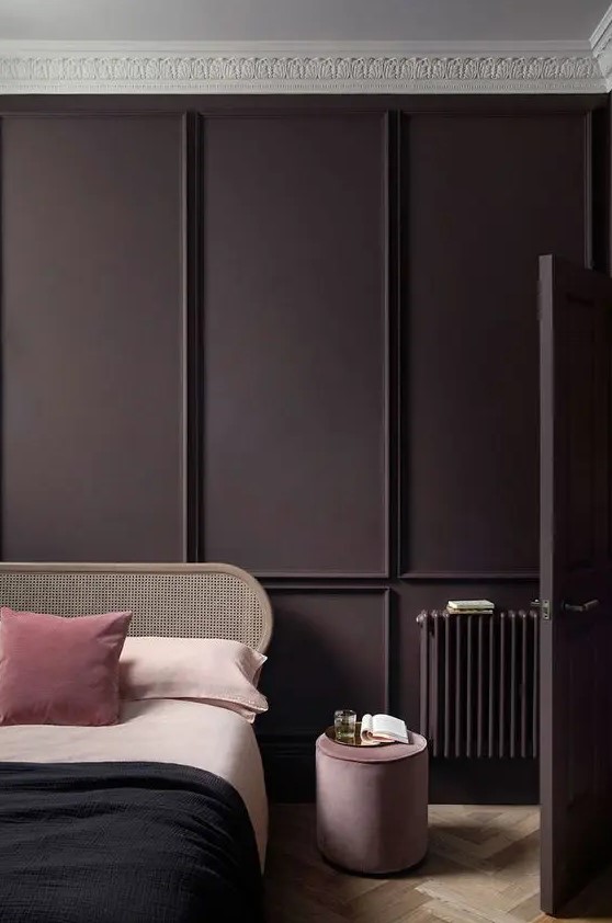 a refined modern bedroom with an aubergine paneled wall and door, a parquet floor, a chic bed and blush and purple bedding