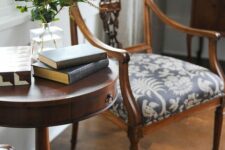 a refined nook with a dark-stained round table and a chic antique chair with printed upholstery, some books and greenery