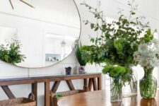 a rustic entryway with a wooden console and table, with baskets, an oversized round mirror and lots of greenery