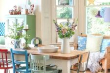 a shabby chic dining space with a loveseat at the bay window, a stained table and mismatching colorful and pastel chairs, an aqua pendant lamp