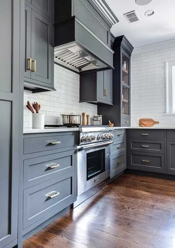 a slate grey kitchen with shaker cabinets, white skinny tiles and a white stone countertop plus a stained wood floor