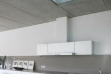 a sleek minimalist white kitchen with lots of cabinets and a concrete backsplash and countertops plus a skylight