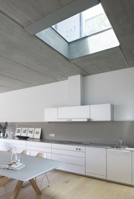 a sleek minimalist white kitchen with lots of cabinets and a concrete backsplash and countertops plus a skylight