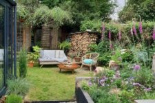a small and cozy garden with a flower bed, some bright blooms in pots and not only, a lawn and some garden furniture