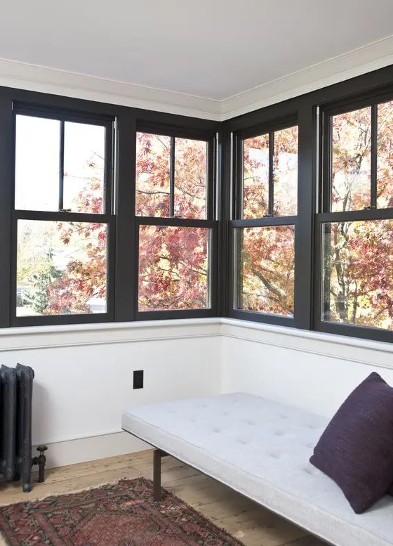 a small and cozy sunroom done with rows of double-hung windows with black framing and a cozy daybed