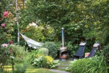 a small garden with a green lawn, greenery, blooms, shrubs and trees, a hearth, some loungers and a hammock
