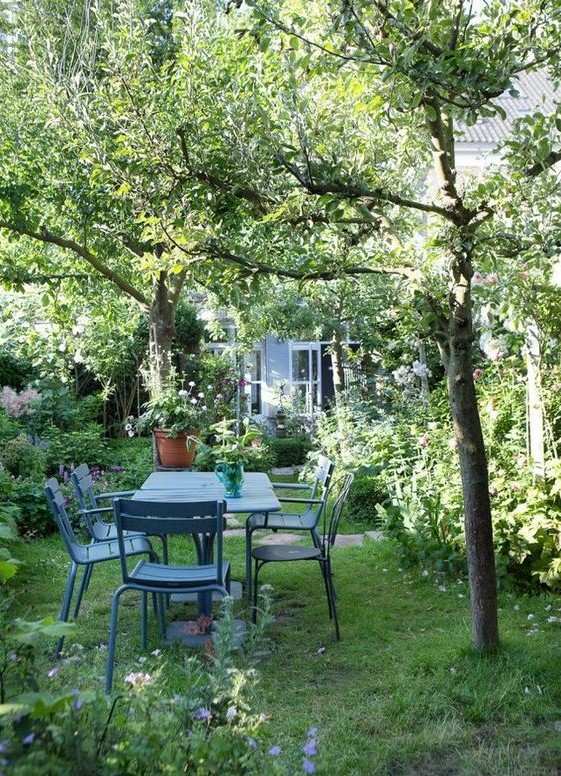 a small garden with a green lawn, some trees, lots of shrubs, trees and a blue garden dining set plus blooms