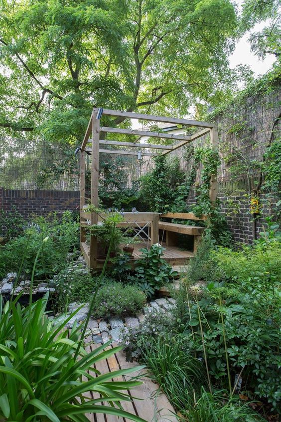 a small garden with a wooden terrace, greenery and blooms, a stone and wooden pathway is a lovely space to be in