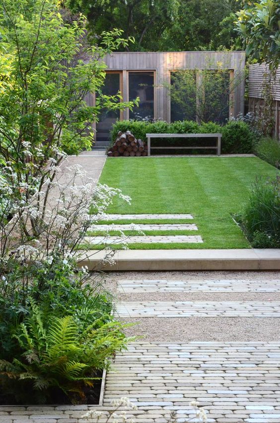 a small minimalist garden with a gravel and brick pathway, a green lawn, shrubs and trees is a stylish and edgy space