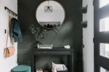 a small modern entryway with a dark green geometric wall, a black console, a green ottoman and potted greenery