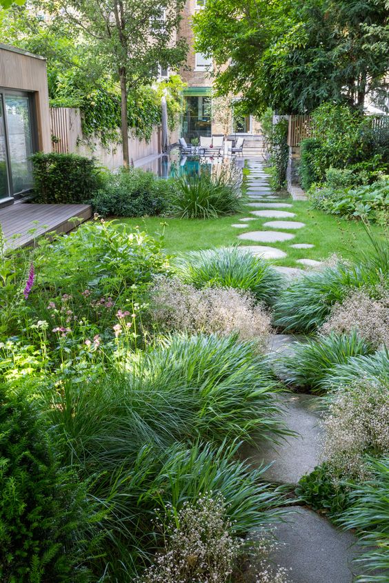 a small modern garden with lawn and greenery, with trees and a swimming pool, with blooms and stones is a cool space