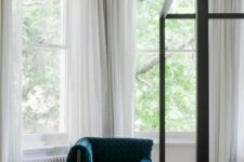 a sophisticated bedroom with arched double-hung windows, a black canopy bed, a teal chair and a side table