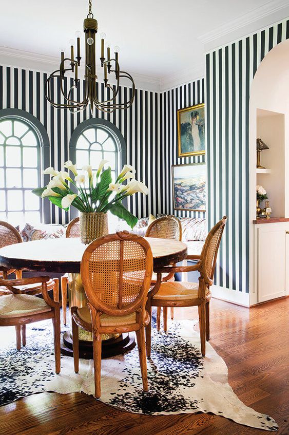 a sophisticated dining space with striped walls, a round table and vintage chairs, a black chandelier and some art