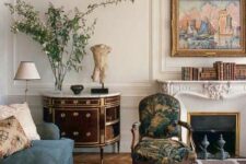 a sophisticated interior with a French fireplace, a blue sofa, a refined antique chair and a sideboard, books and art