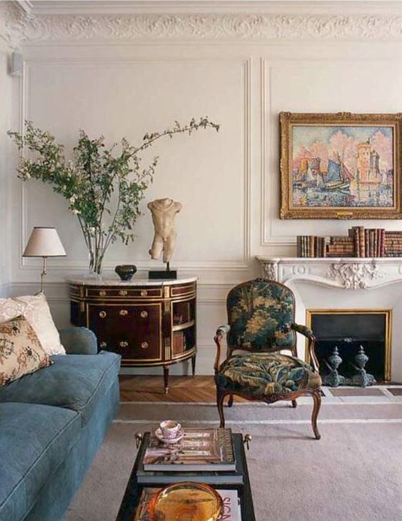 a sophisticated interior with a French fireplace, a blue sofa, a refined antique chair and a sideboard, books and art