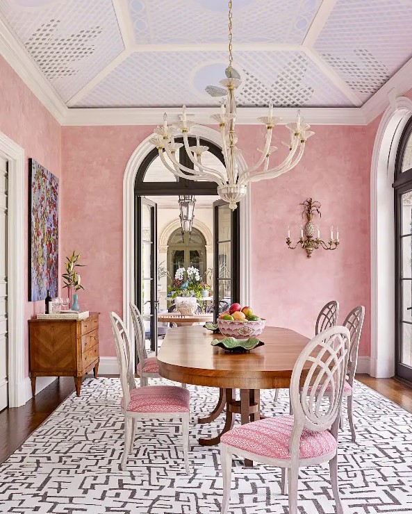 a sophisticated pastel pink dining room with a stained credenza, an oval table, pink chairs, a bold artwork and a printed rug
