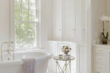 a sophisticated vintage bathroom with a double-hung window, built-in cabinets, an oval tub and a side table