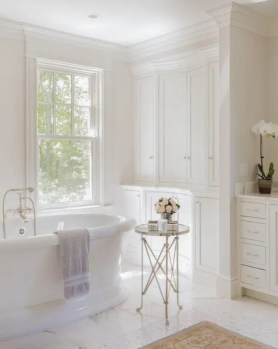 a sophisticated vintage bathroom with a double-hung window, built-in cabinets, an oval tub and a side table