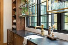 a stained kitchen with black stone countertops and brass suspended shelves over the windows is a cool and elegant space