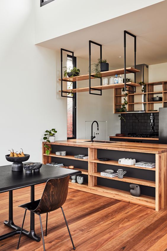 a stylish kitchen in black and light-stained wood, with open cabinets and suspended shelves, a storage kitchen island and potted greenery