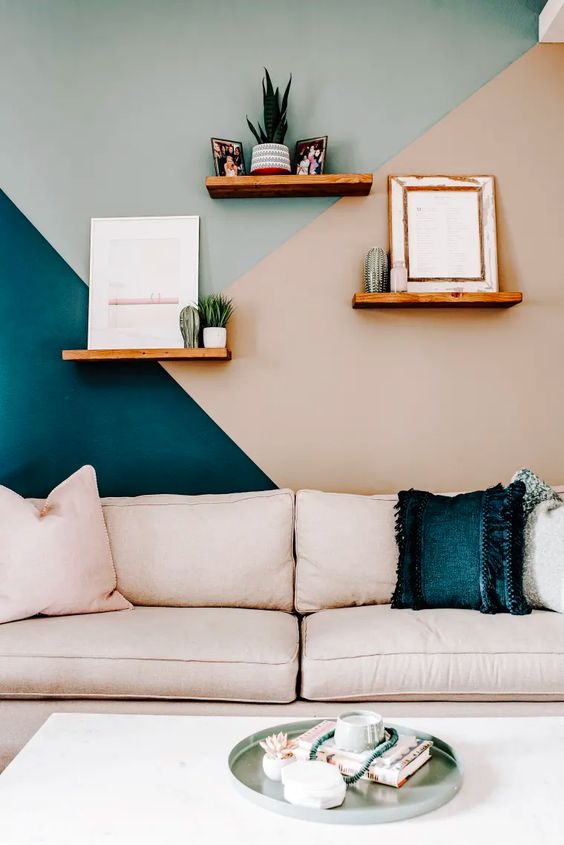 a stylish living room with a color block geo accent wall in teal, aqua, blush, a blush sofa and pillows, open shelves