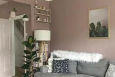 a stylish mauve living room with a grey sofa, a shelf and a floor lamp, some plants and a wooden pendant lamp
