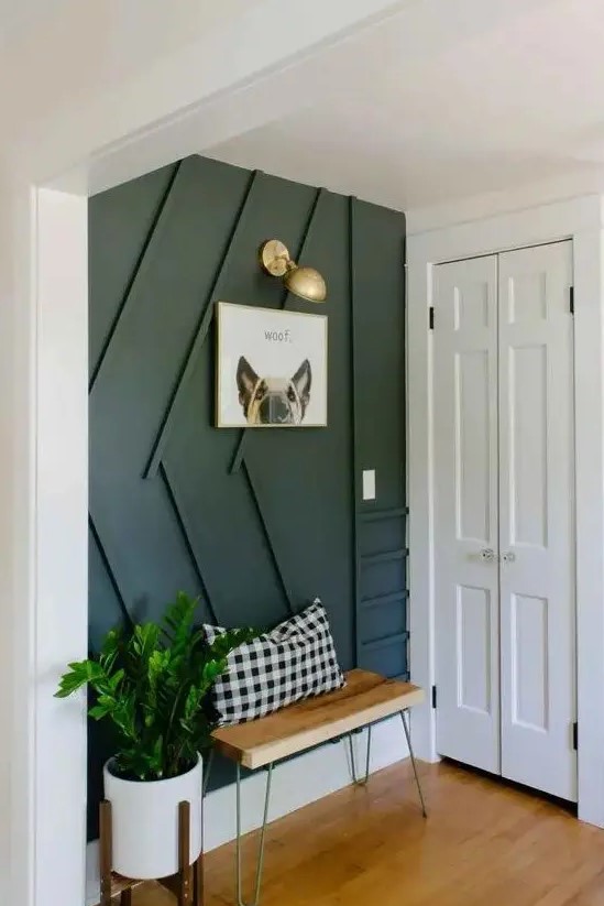 a stylish modern entryway with a black paneled wall, a small bench, a sconce and potted greenery is very cool