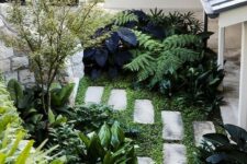 a tiny garden nook with greenery, lots of various shrubs and a small tree plus stone paves