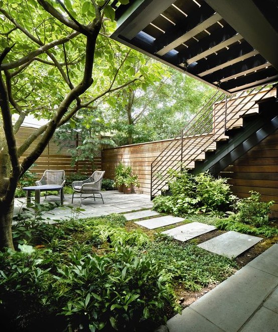 a townhouse garden with stone tiles, potted greenery and trees plus rustic furniture