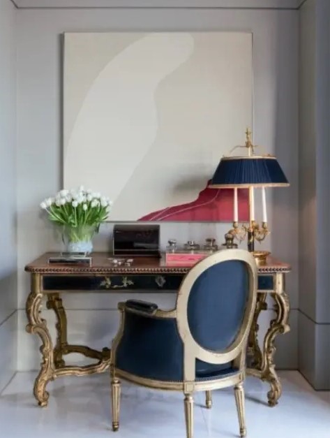 a vintage working nook with a statement print, a vintage black and gold desk, an antique navy and gold chair and a matching table lamp
