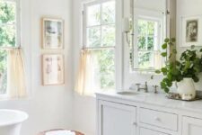 a white farmhouse bathroom with marble hex tiles, double-hung windows, an oval tub, a large vanity and a window cabinet