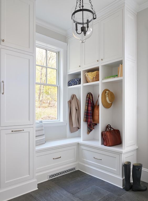 a white farmhouse mudroom with a double-hung window, shaker style cabinets and a vintage pendant lamp is cool and airy